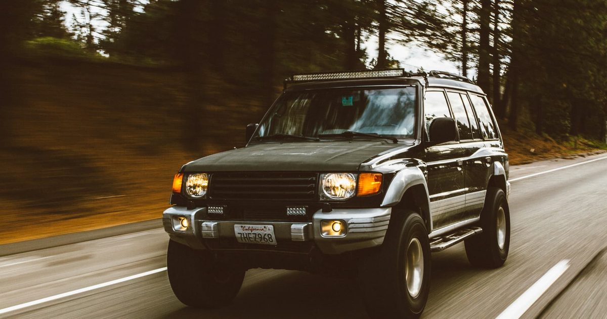 Dark Toyota SUV with a roof rack driving along a forest road