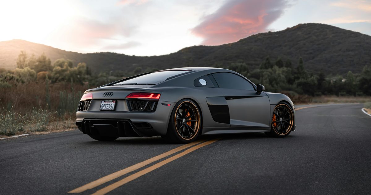 Gray Audi R8 photographed from the rear three-quarter angle on a mountain road at sunset