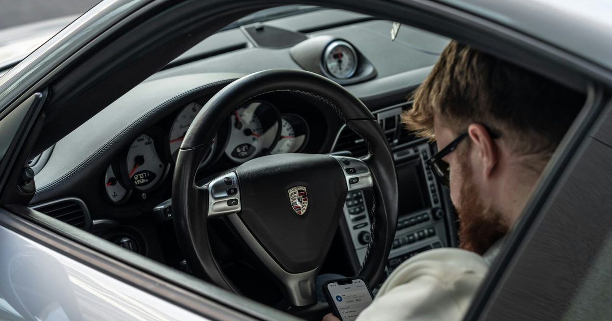 View through a Porsche window showing the steering wheel, dashboard and a seated man